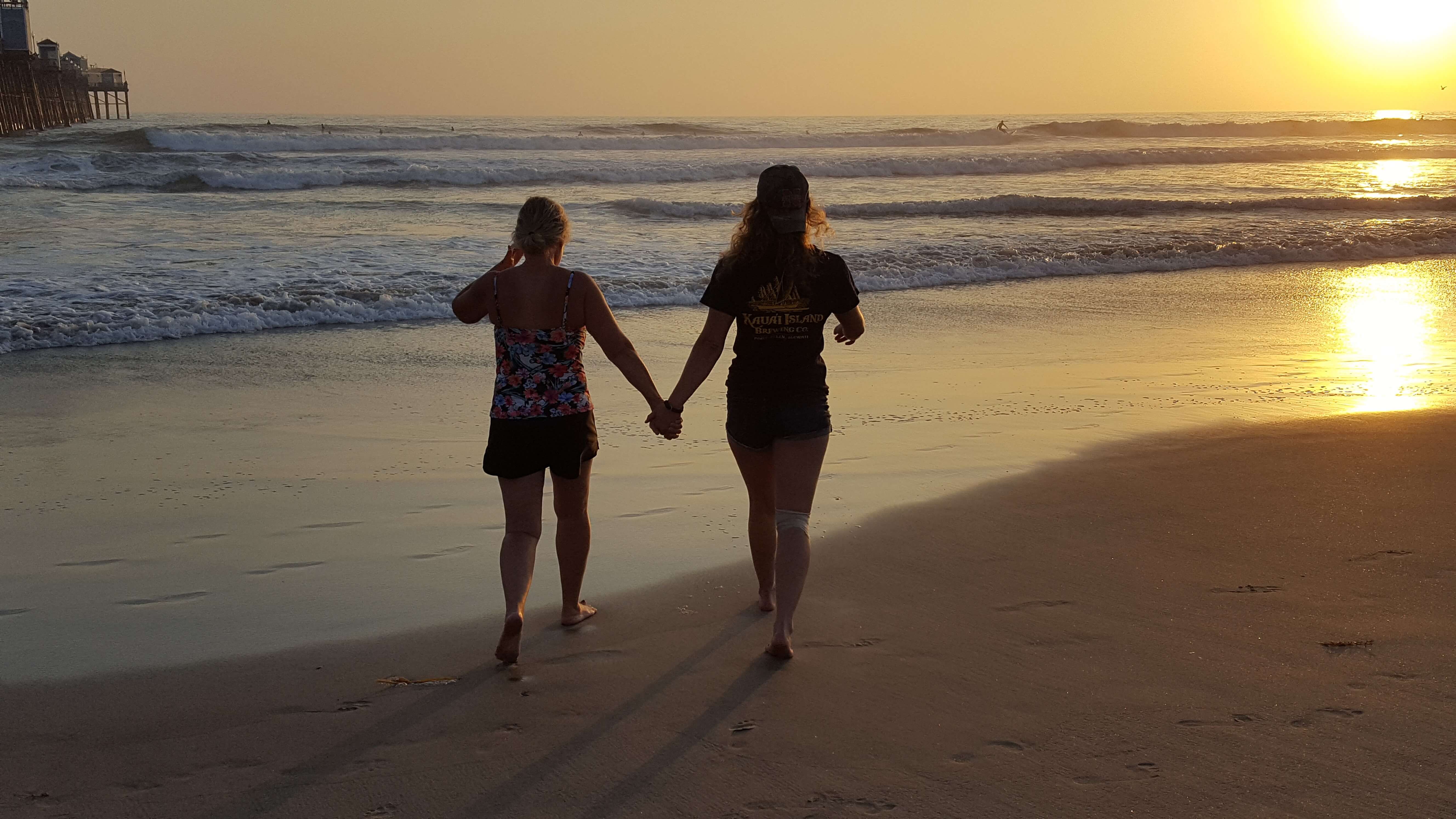 Mom and daughter walking on the beach at sunset